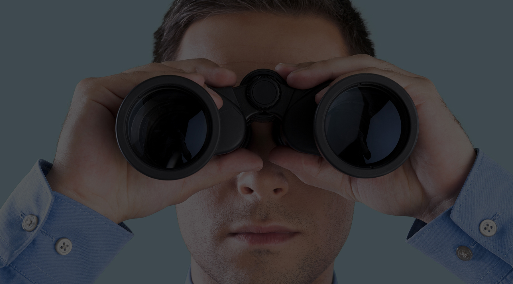 Man in a blue shirt looking ahead through binoculars